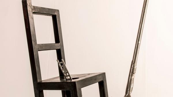 sculpture depicting a chair, spade and miniature ladder balanced upon each other. 