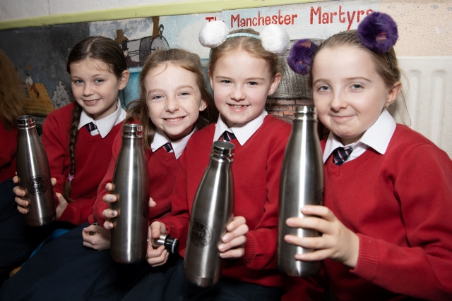 A young group of school children holding refillable water bottle in a class room