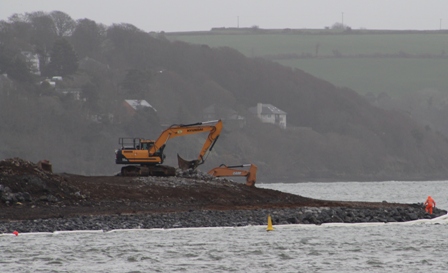 A digger installing rock armour on the coast