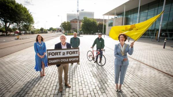 The Mayor of the County of Cork standing outside the County hall holding a yellow flag promoting the fort to for cycle charitty