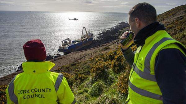 Council staff operating walkie talkies, with helicopter lifting barrels from wreck