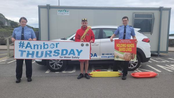 A lifegaurd and two Gardaí holding signs promoting amber thursday