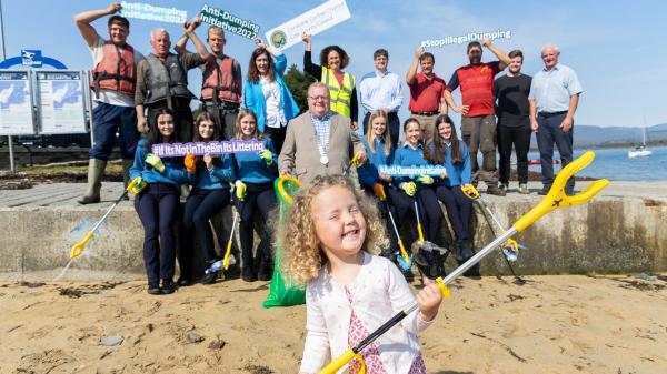 The Mayor with a group of school children at a beach holding anti litter signs with a young child in the foreground hold an anti litter picker.