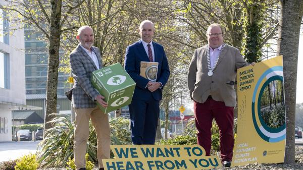 Three people standing in a open space with holding promotional Material