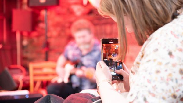 A girl taking a picture of a musician on a smartphone.