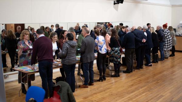 A group of people standing opposite each other on a long table taking part in a Speed Networking event.