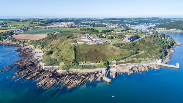 An aerial view of a fort on a green hill with a body of water