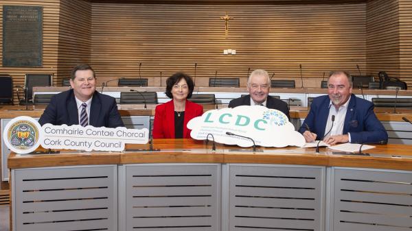 4 people in Cork County Council chamber holding the Cork County Council logo and the Local Community Development Committees  logo.