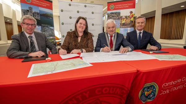 Four people signing a contract at a table with Cork County Council branding in the background.