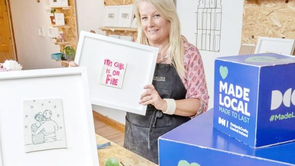 Cork County Council Invites Applications for Creative Startup Scheme 2024. Pictured is a lady holding handmade products alongside a box shaped sign saying 'Made Local, made to last.'