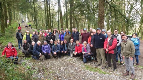 A group of approximately 30 people in a forrest surrounded by trees.