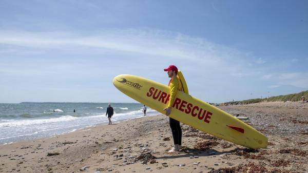 A Cork County Council beach lifeguard holding a surf rescue board looking out towards the sea.