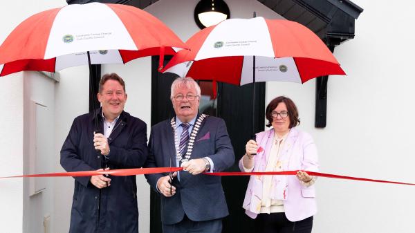 3 people holding umbrellas and cutting a ribbon