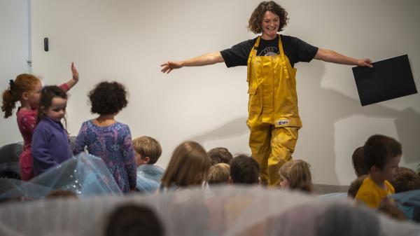 Woman standing in front of a group of children reading them a story.
