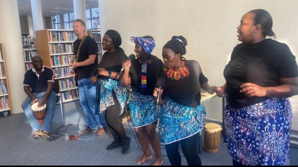 Six people in a library singing, dancing and playing instruments inclusing a guitar and drums.