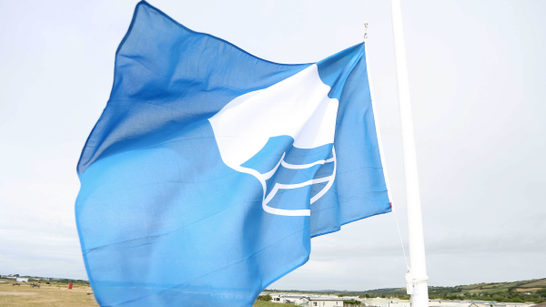 A blue flag flying with a shy and beach dunes in the background