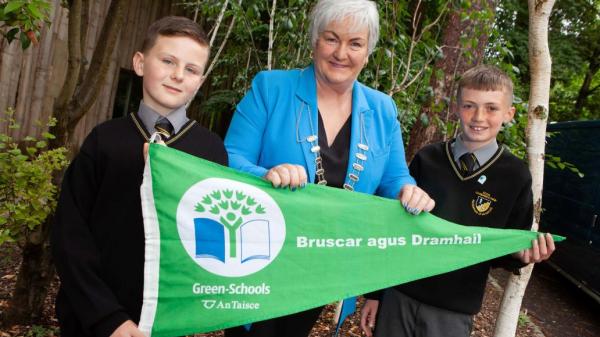 One adult and two children holding green flag with trees in the background.