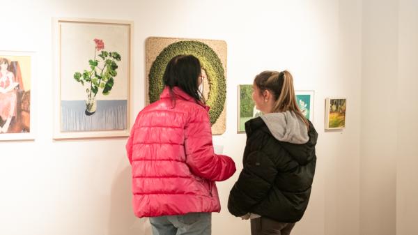 Two women looking at pictures on a white wall.
