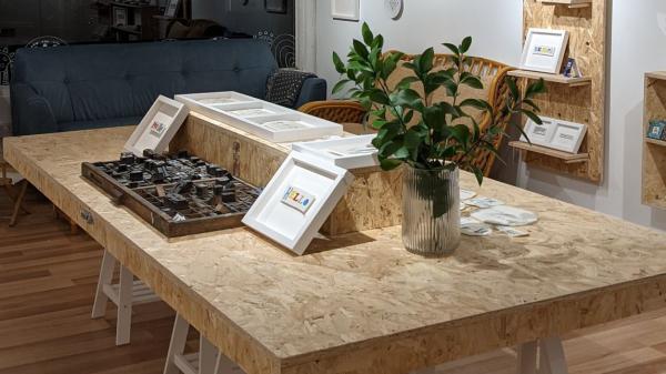 Wooden table with plant and pircture frames on it on wooden floor. Picture frames also cover the walls which are white and black.