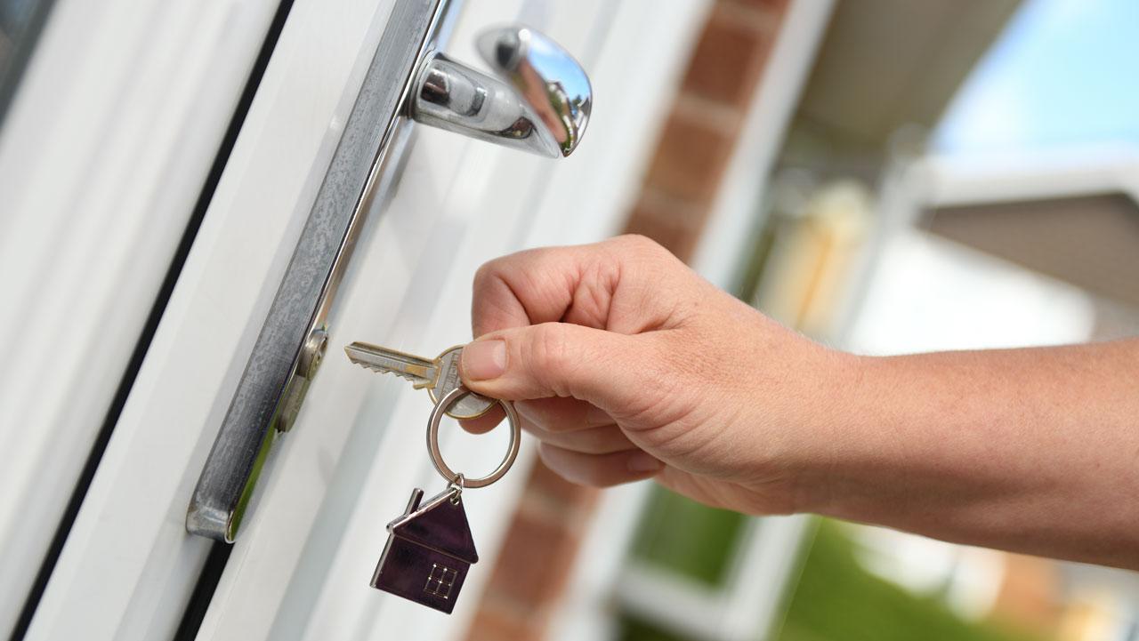 A person holding a key about to open a door lock