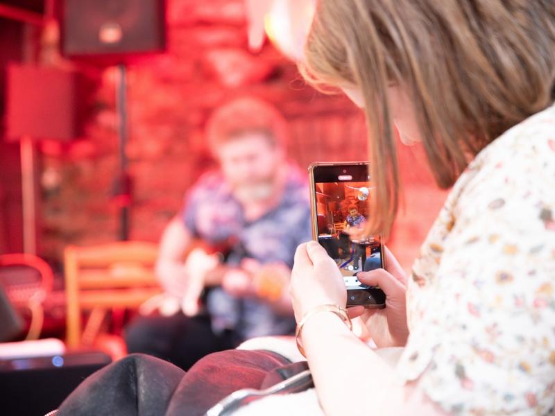 A girl taking a picture of a musician on a smartphone.