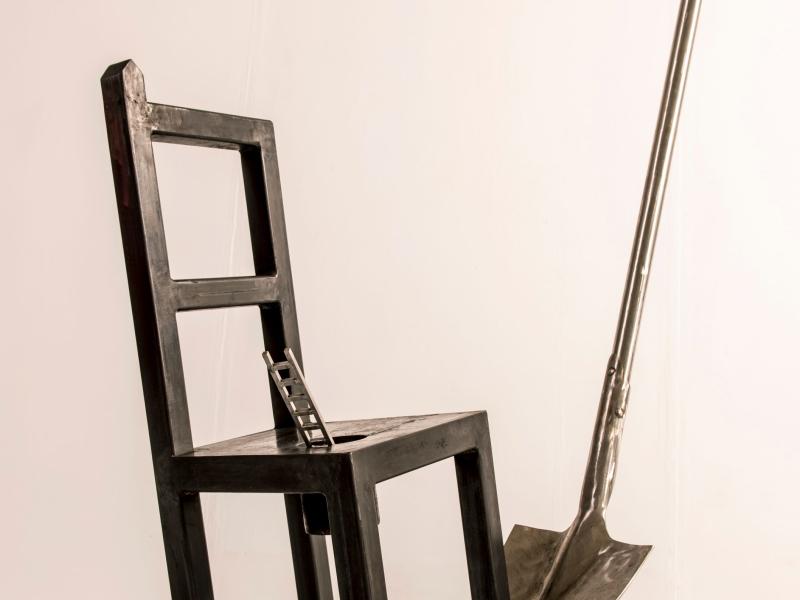 sculpture depicting a chair, spade and miniature ladder balanced upon each other. 