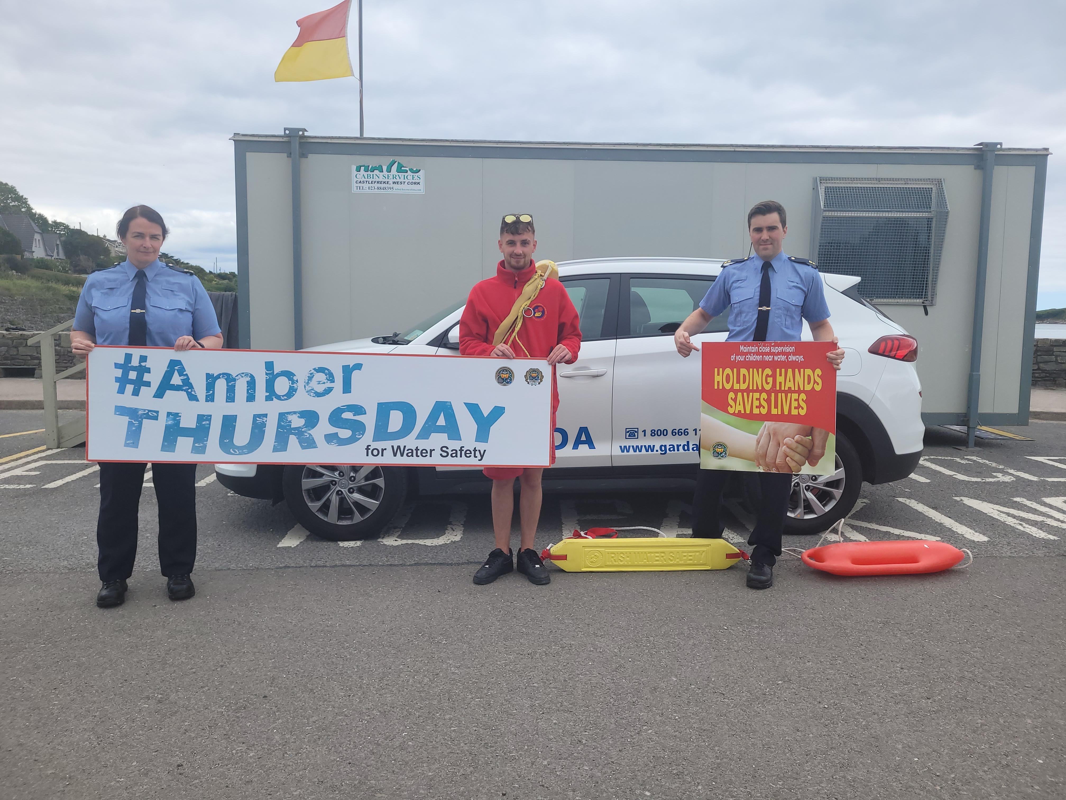 A lifegaurd and two Gardaí holding signs promoting amber thursday
