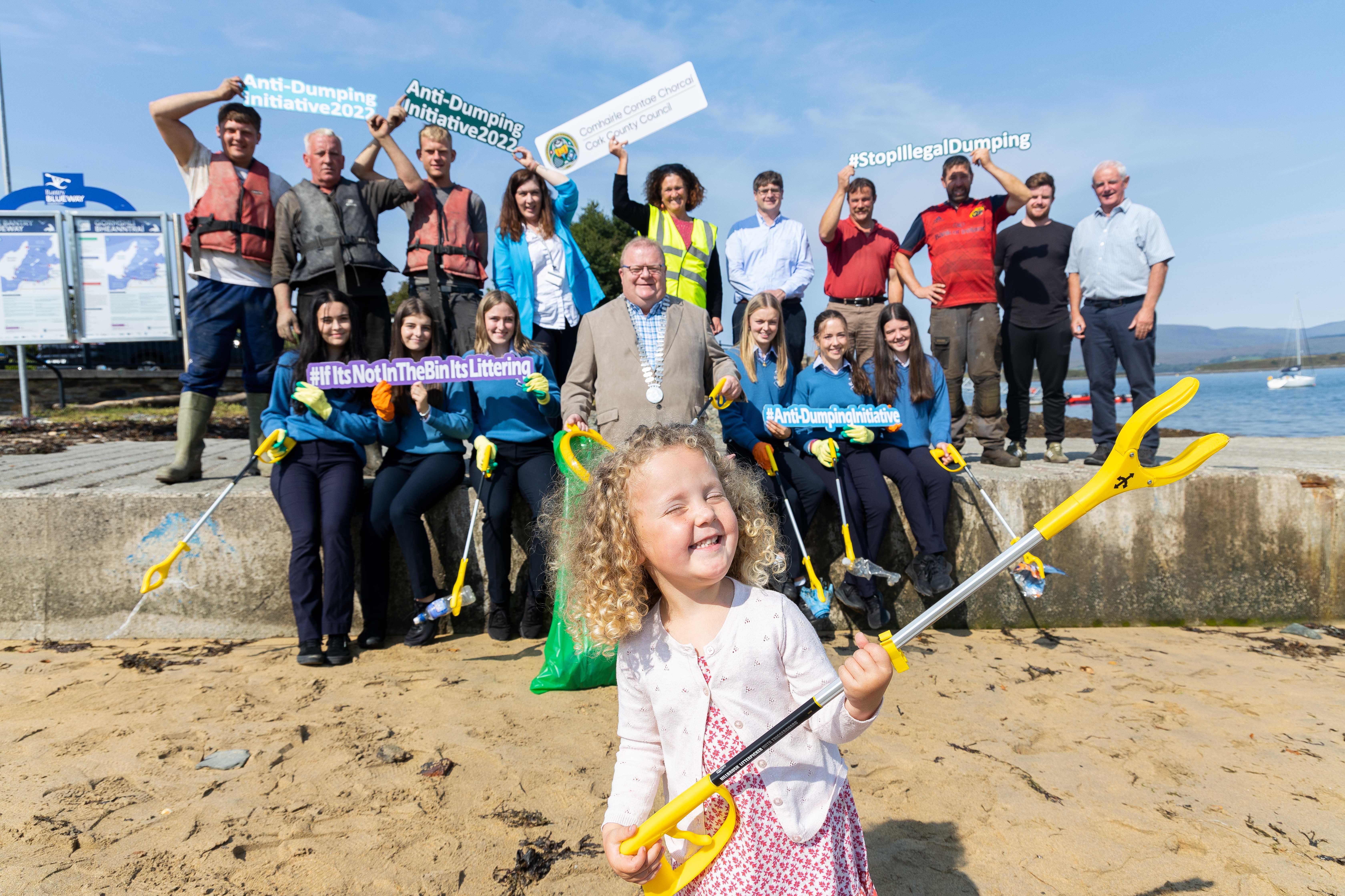 The Mayor with a group of school children at a beach holding anti litter signs with a young child in the foreground hold an anti litter picker.