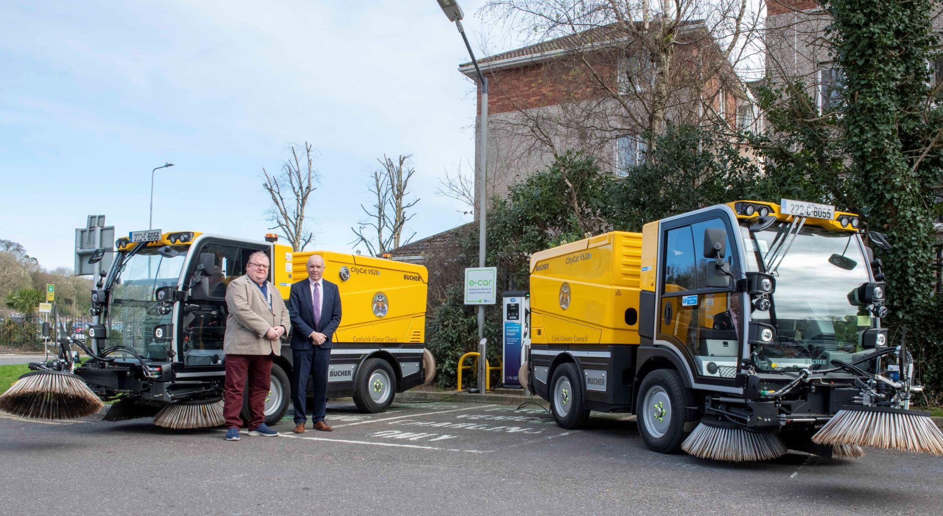 2 men standing next to two sweepers.