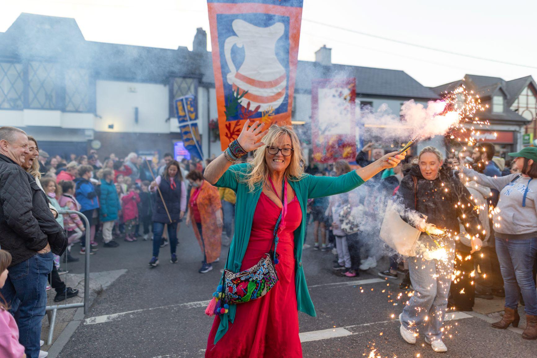 A woman on a crowded street waving a sparkler