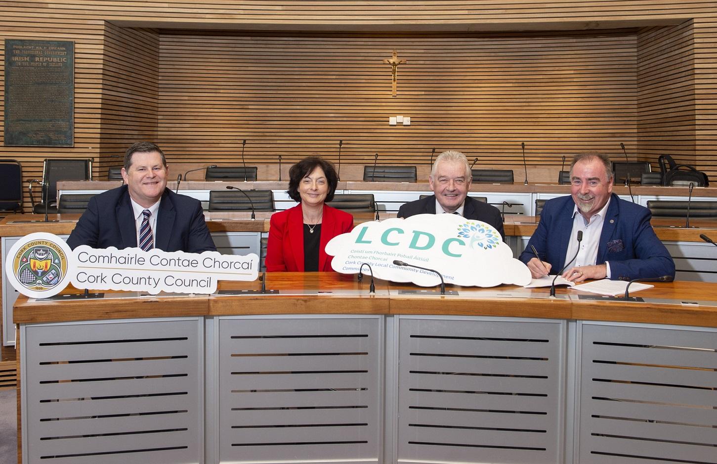 4 people in Cork County Council chamber holding the Cork County Council logo and the Local Community Development Committees  logo.