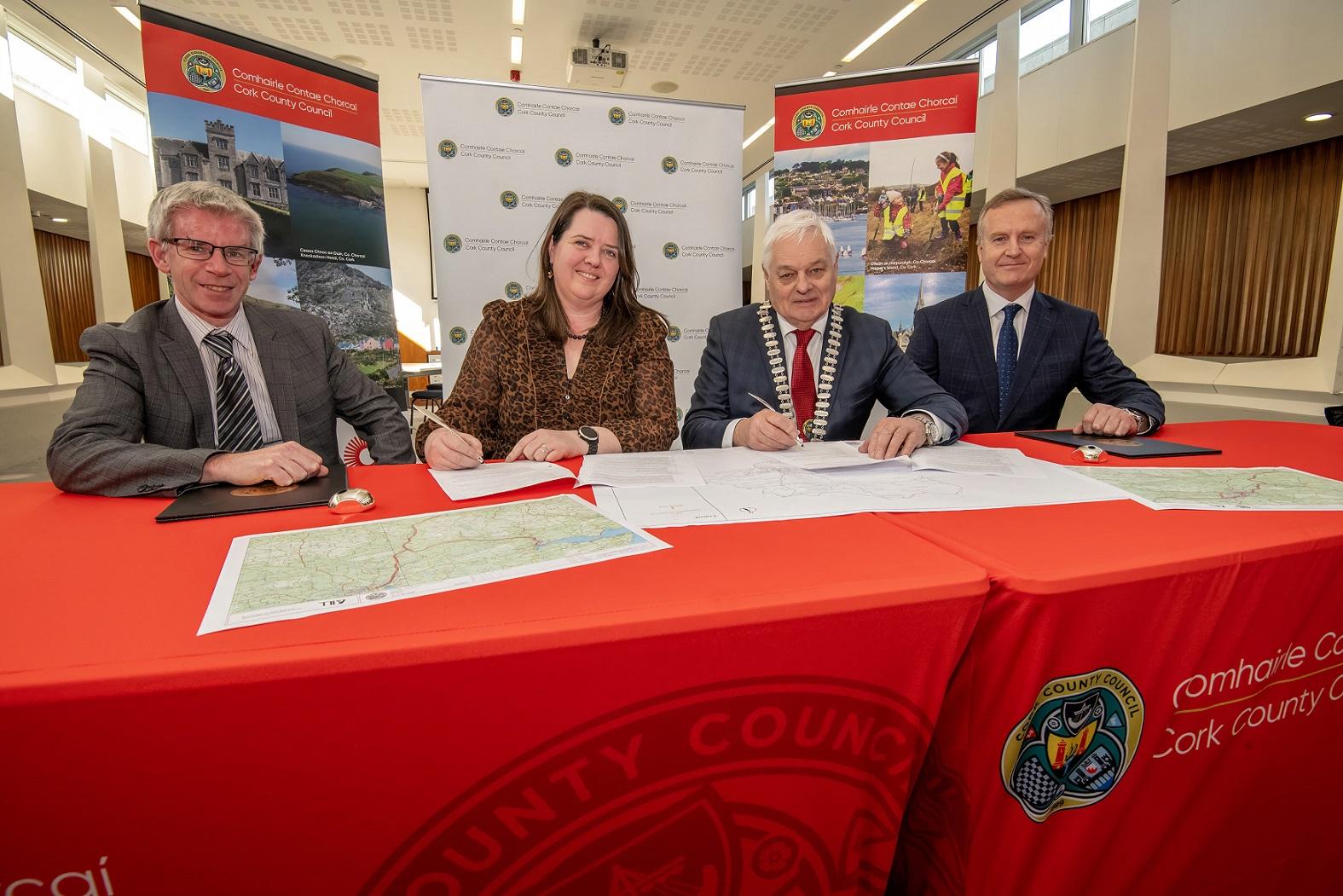 Four people signing a contract at a table with Cork County Council branding in the background.