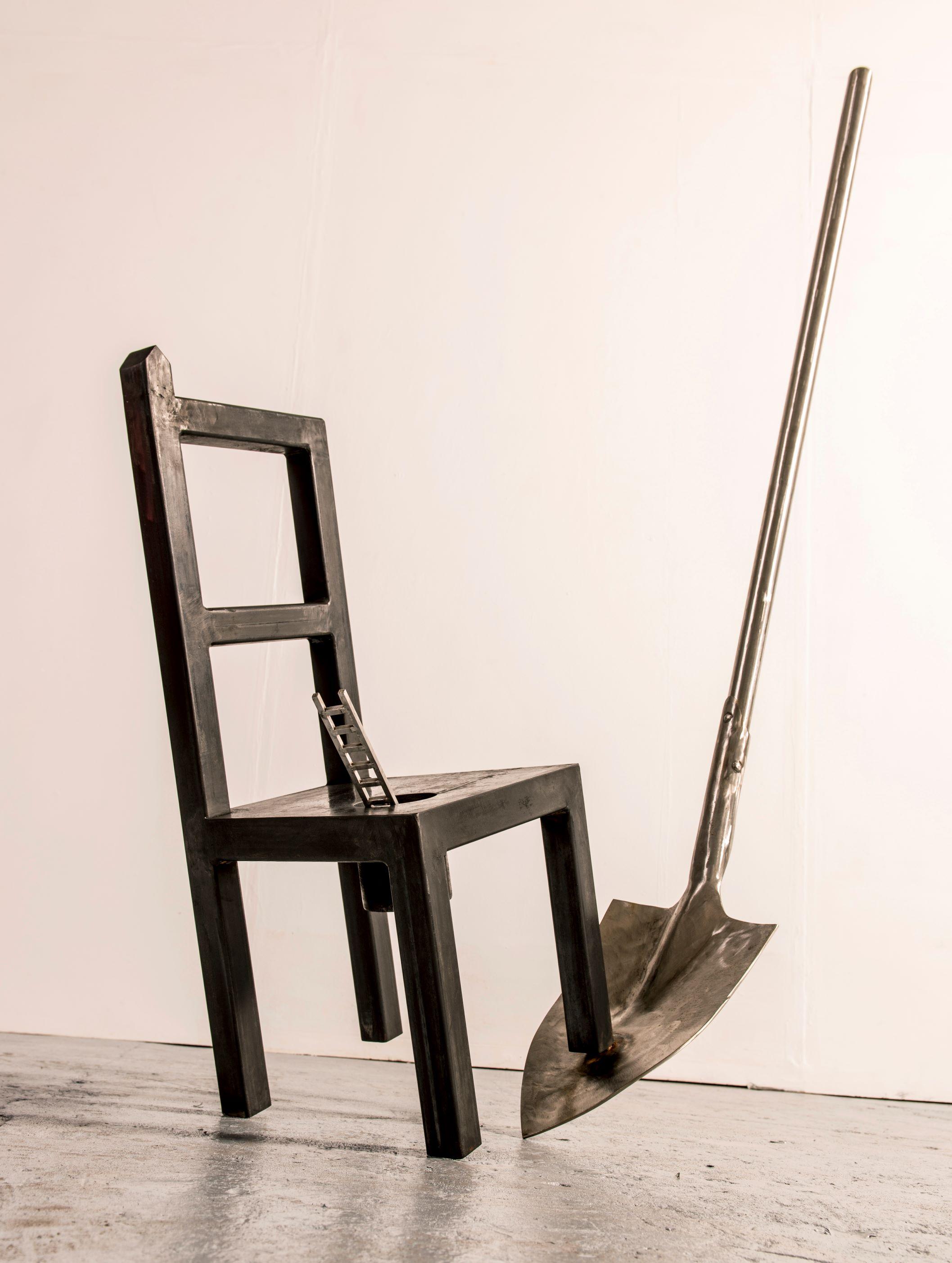 sculpture depicting a chair, spade and miniature ladder balanced upon each other. 