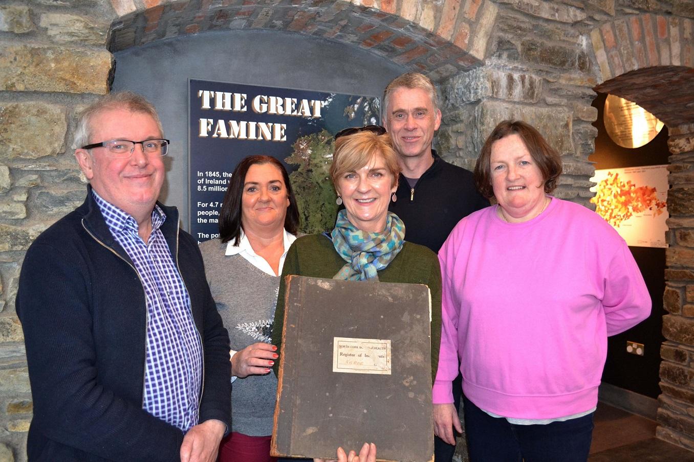 5 people, one of whom is holding a burial register record book.