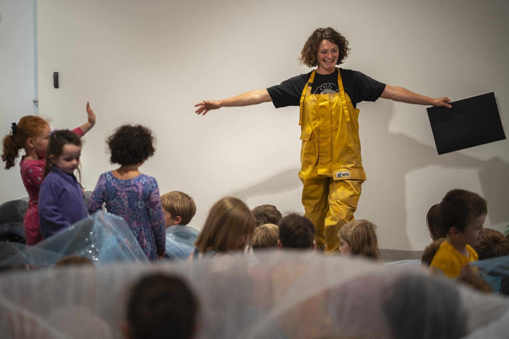 Woman standing in front of a group of children reading them a story.