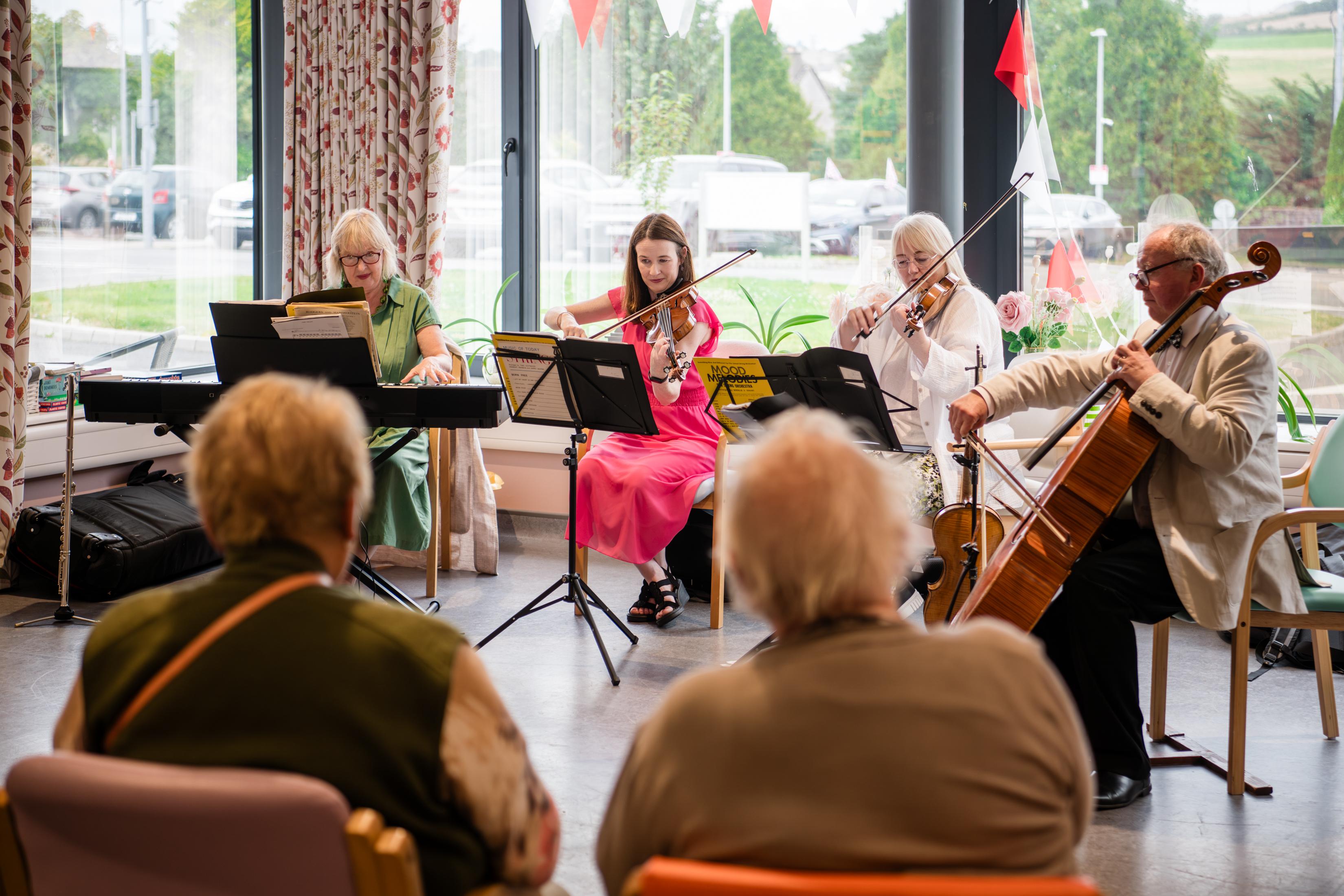 Four people playing instruments while audience listens.