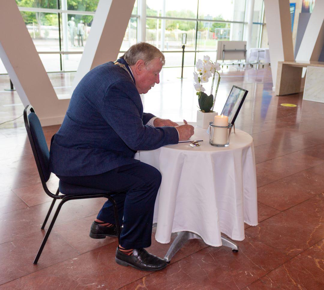 A person sitting at a table signing a book of Condolence.