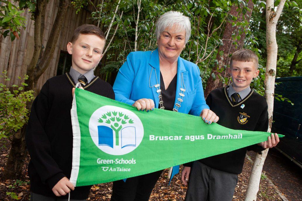 One adult and two children holding green flag with trees in the background.