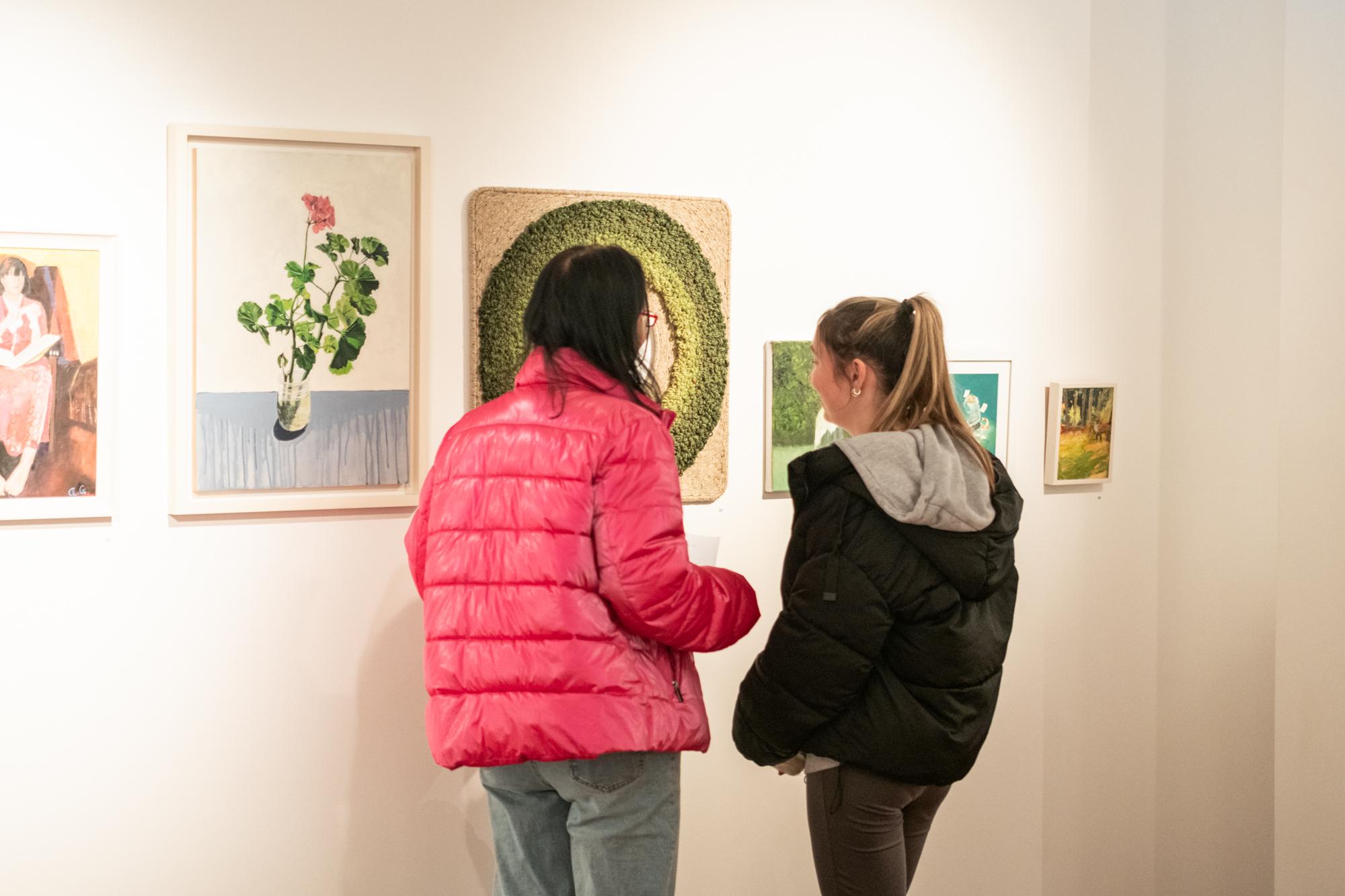 Two women looking at pictures on a white wall.