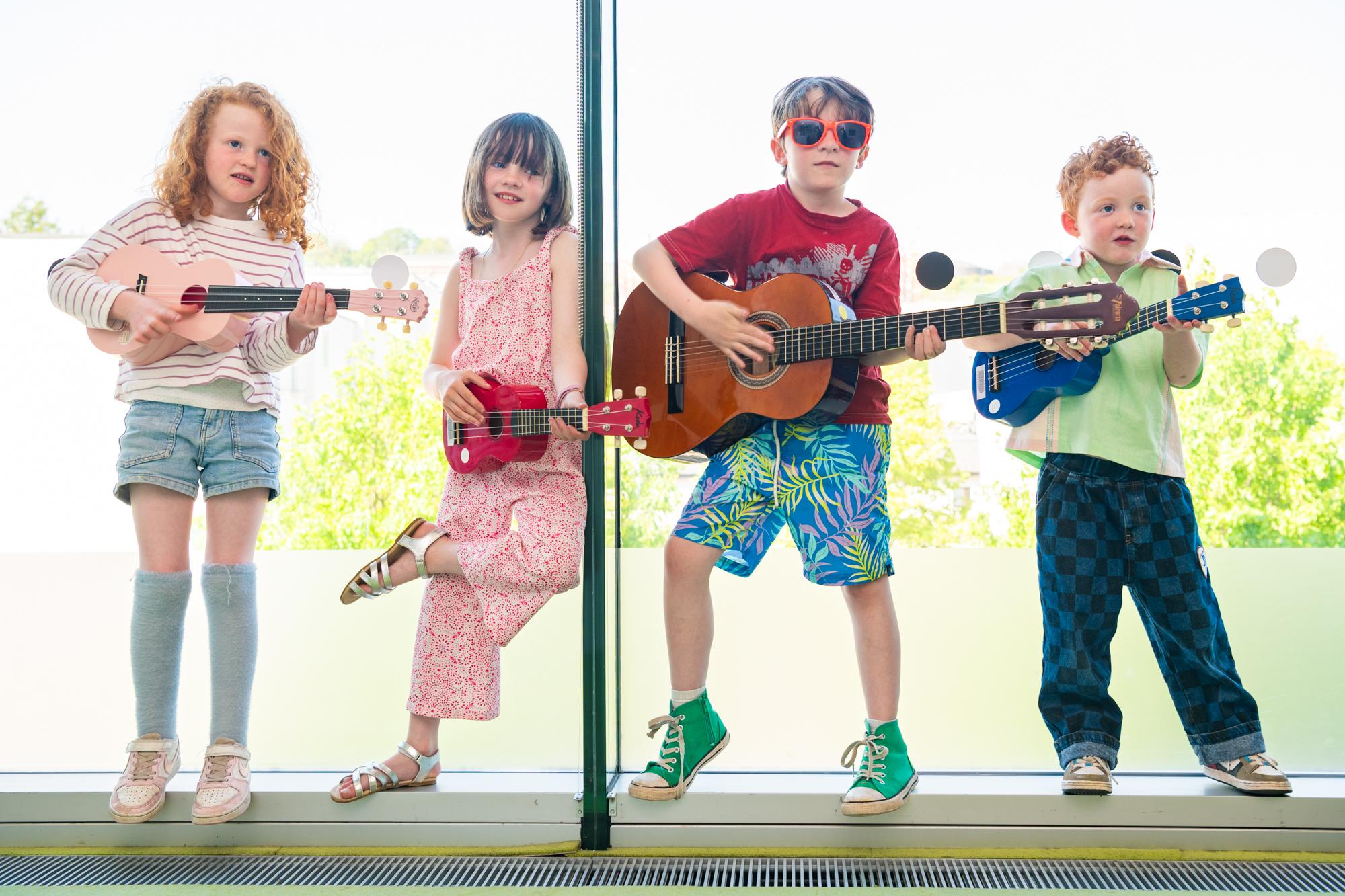 Four children standing in Window playing guitars.
